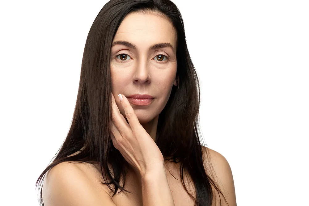 A woman with long dark hair rests a hand against her cheek, her face bare and without makeup